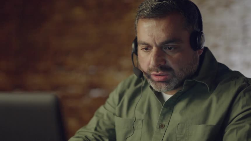 A man wearing a headset works on a computer