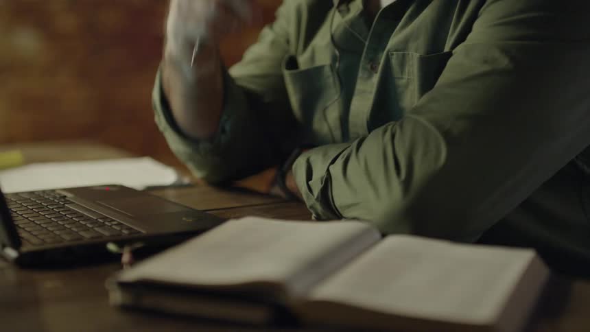 A man working on a laptop checks a book