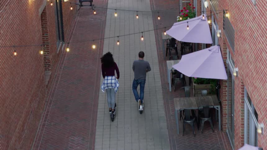 Man and woman ride scooters in a city