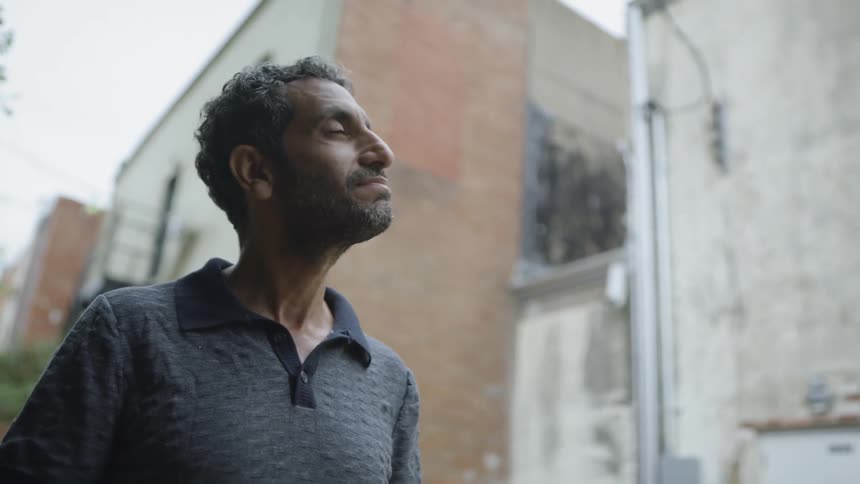 A man holding an open book looks up at a building and nods