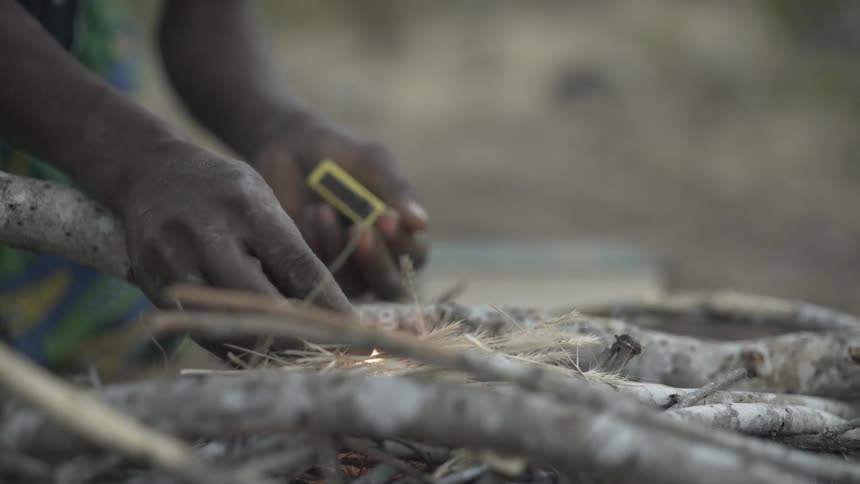A person strikes a match and starts a campfire