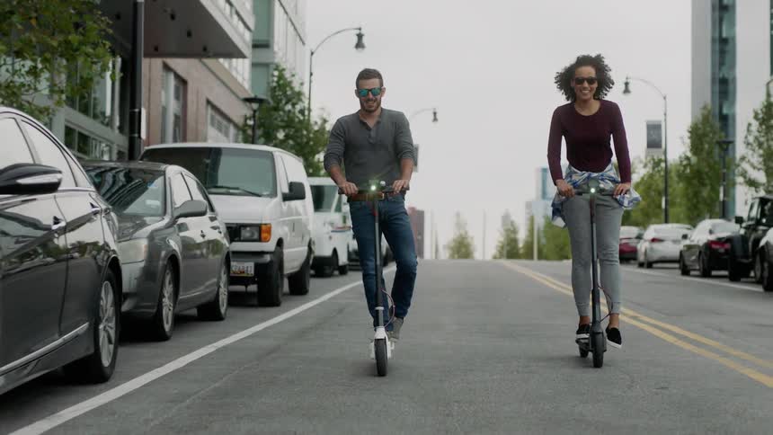 A couple riding scooters down the street