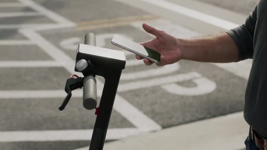 A man rents a scooter on a city street using his phone