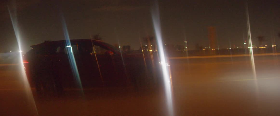A red car is driven down the road at night