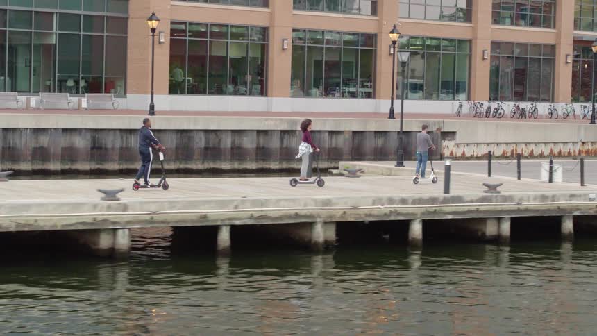 Three people on scooters ride along the pier