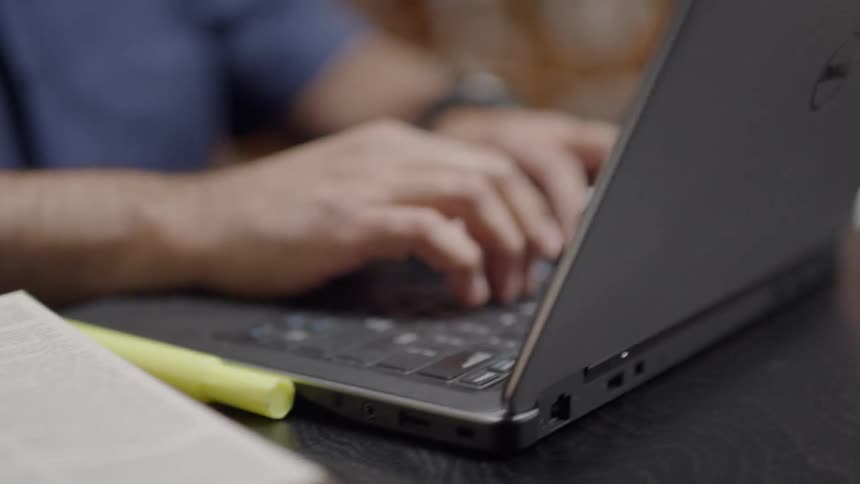 A man reads a book and works on a laptop