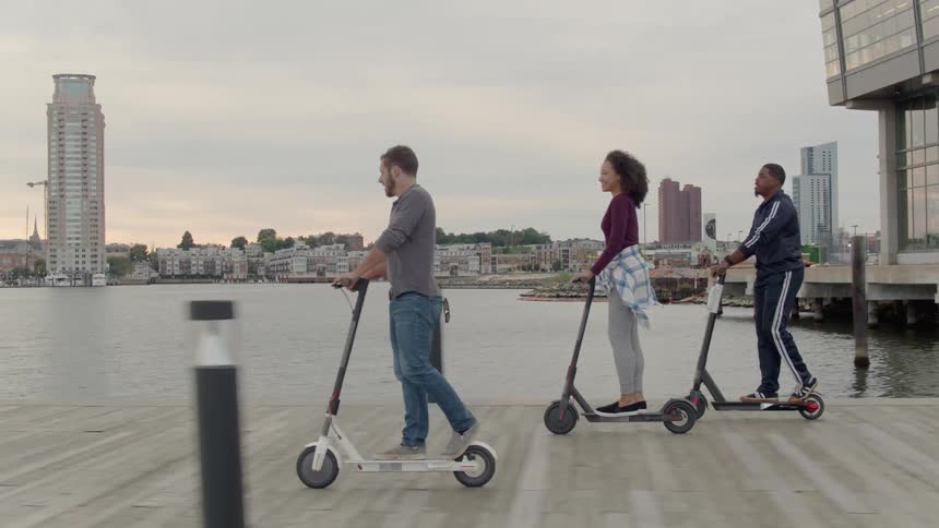 Friends ride scooters on a pier at sunset