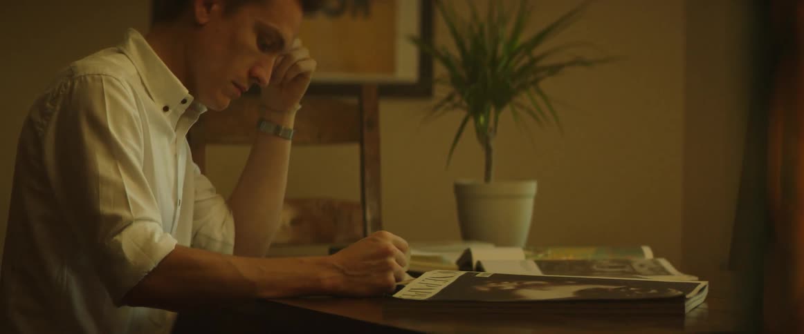 A man is sitting reading at a table inside during the day
