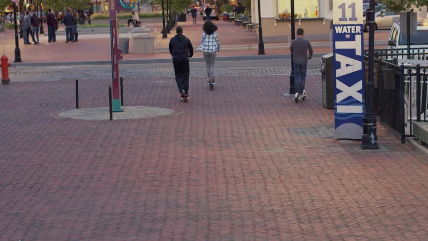 Friends are riding scooters in a plaza in a city at dusk