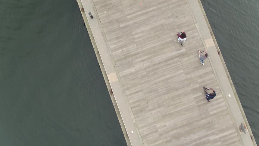 Three people are riding scooters on a pier