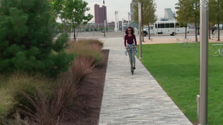 A woman is riding a scooter through a city park during the day