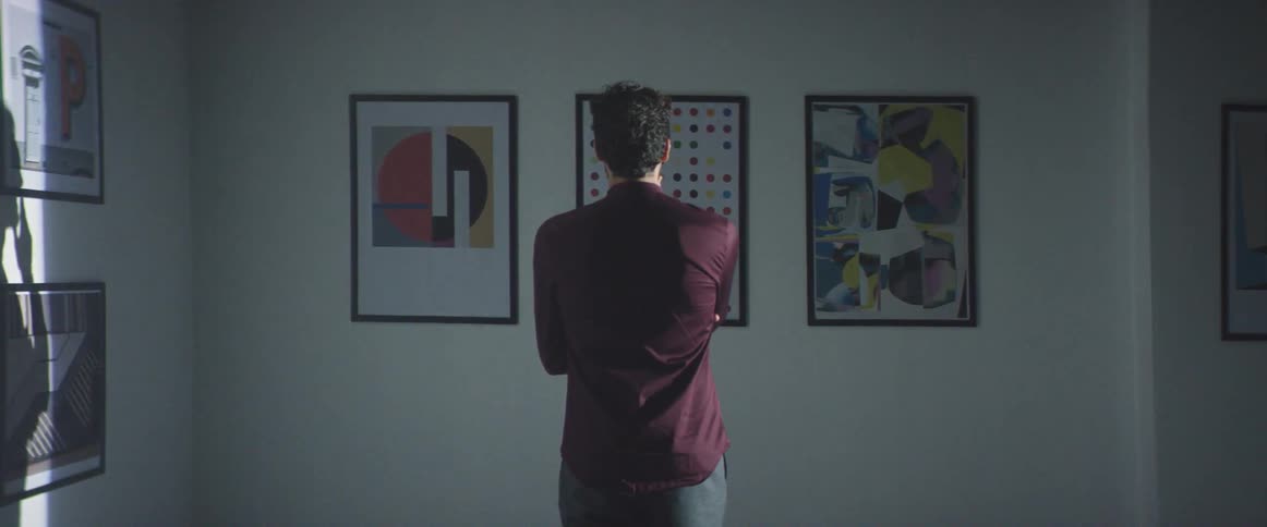 A man is viewing a group of pictures on a wall in a gallery during the day
