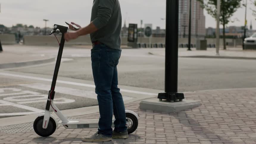 A person gets on a scooter and crosses the street