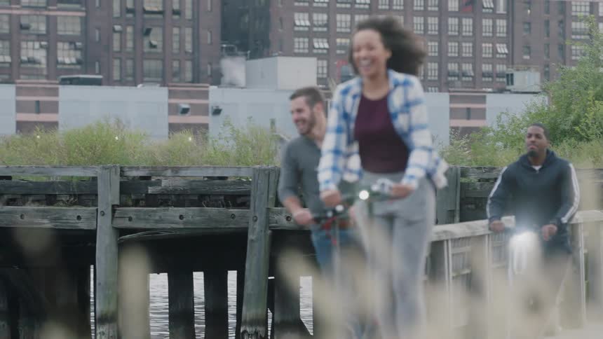 Men and a woman ride scooters outside and laugh