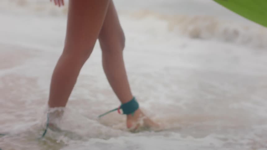 A woman is walking into the ocean holding a surfboard