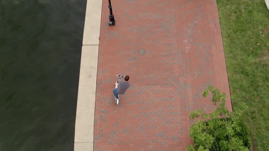 A man rides a scooter on a brick path along the harbor
