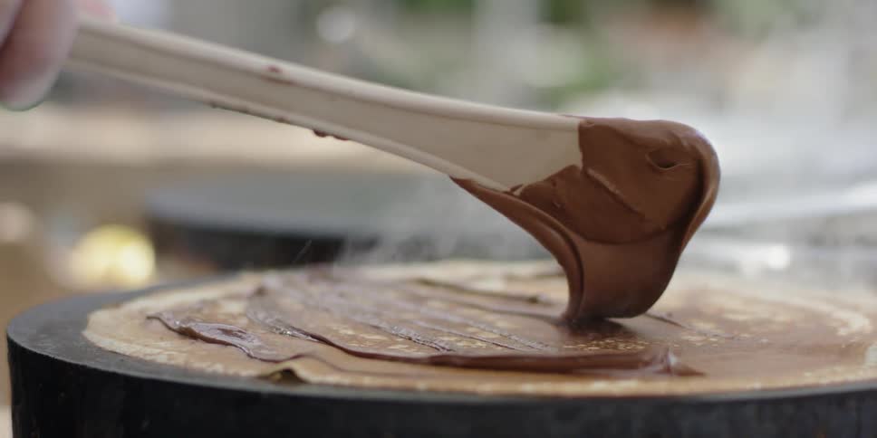A chef spreads chocolate on a crepe