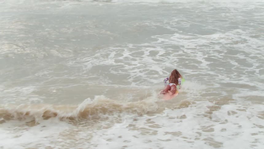A woman paddles out into the water on a surfboard