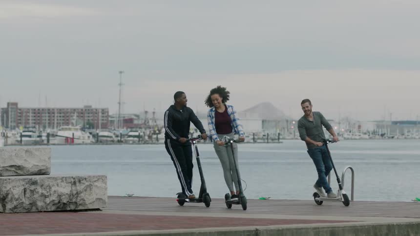 Three people are having fun riding their scooters by the water