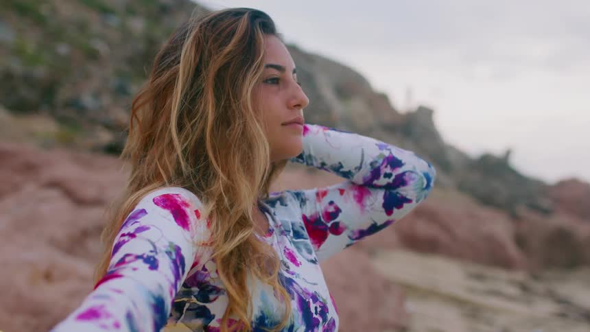 A woman on the beach brushes her hair back with her hand