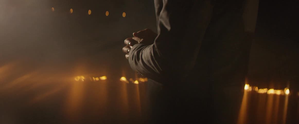 A man stands with his hands clasped near burning fires
