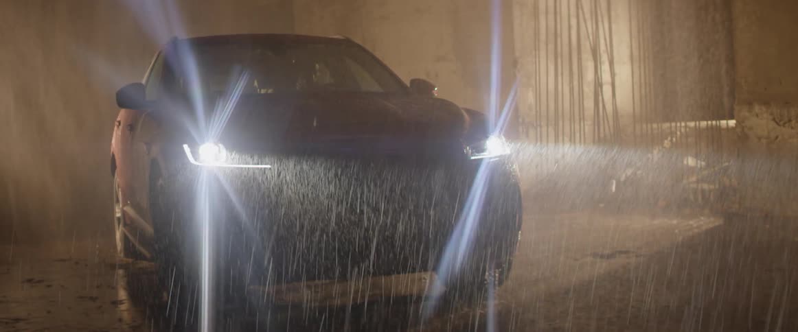 A driver turns his headlights on while sitting in a car in the rain