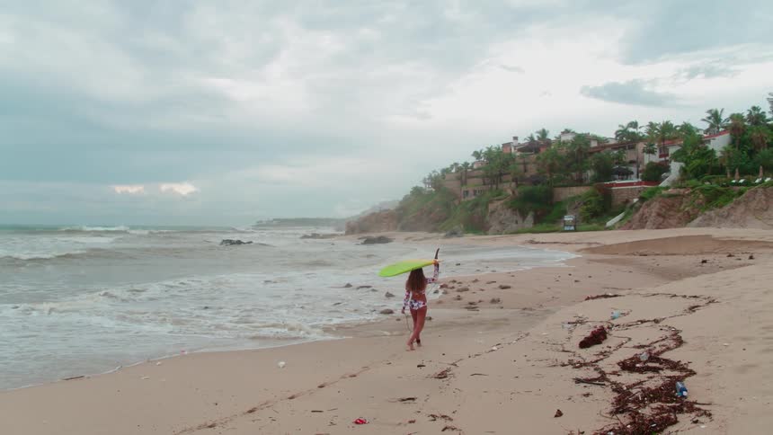 A woman carries a surfboard on the beach