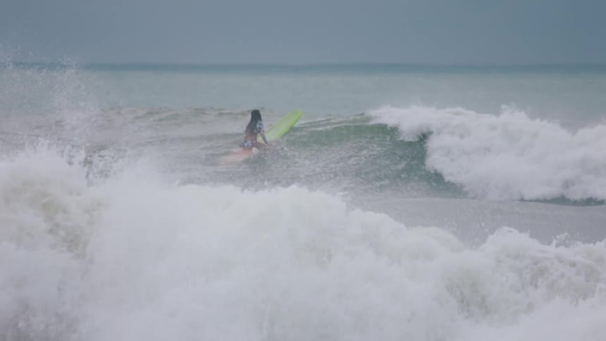A woman sitting on her surfboard rides the waves