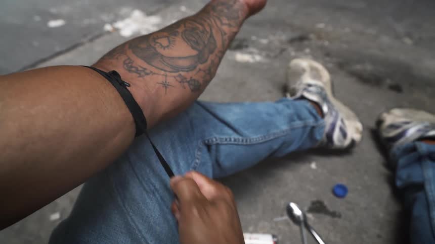 A man ties a string around his arm to inject drugs