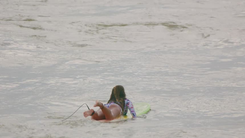 A woman on a surfboard paddles out into the ocean