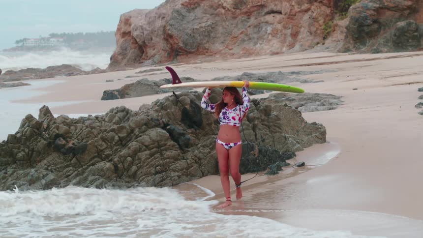 A woman is carrying a surfboard on her head as she walks into the surf during the day