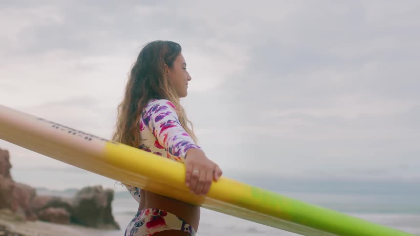 A woman holds a surfboard and looks at the ocean