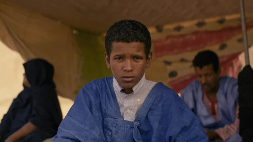 A boy sit next to his family under a haima tent
