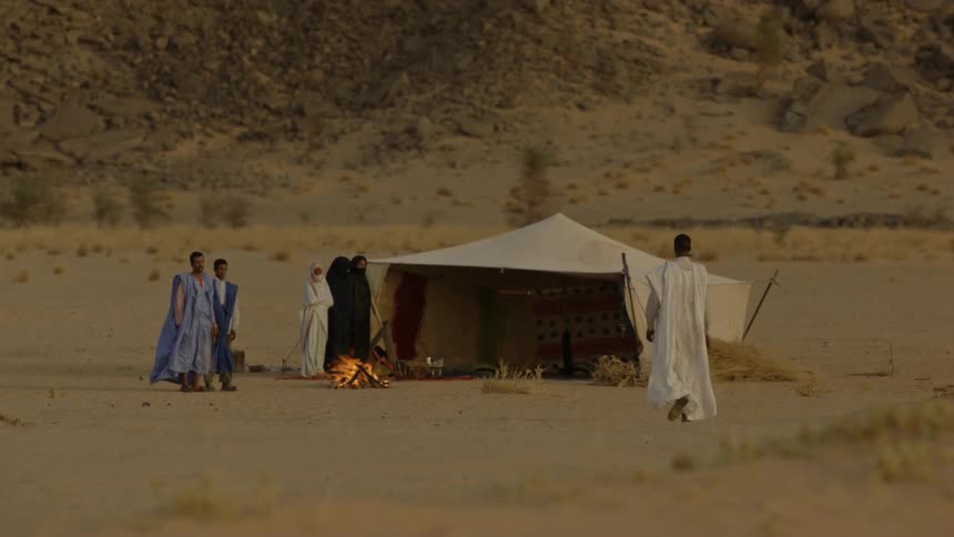 A man is walking toward a waiting group of people near a bedouin tent at dusk