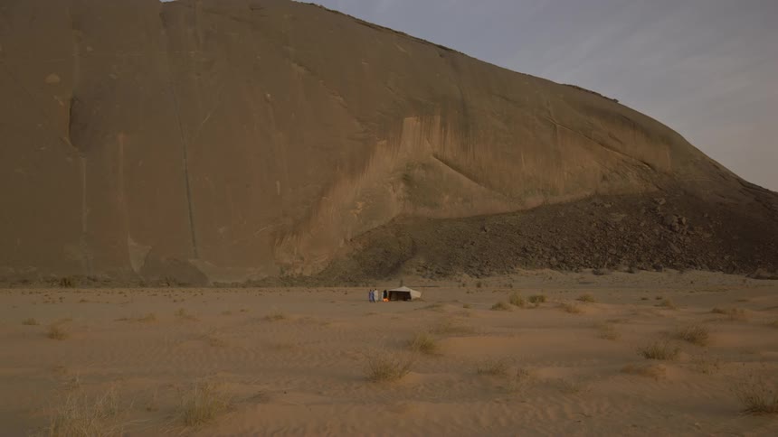 A man is walking toward a tent and other people in a desert at dusk
