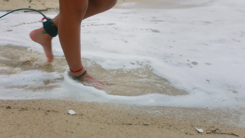 A woman walks barefoot along the beach with a cord attached to her ankle