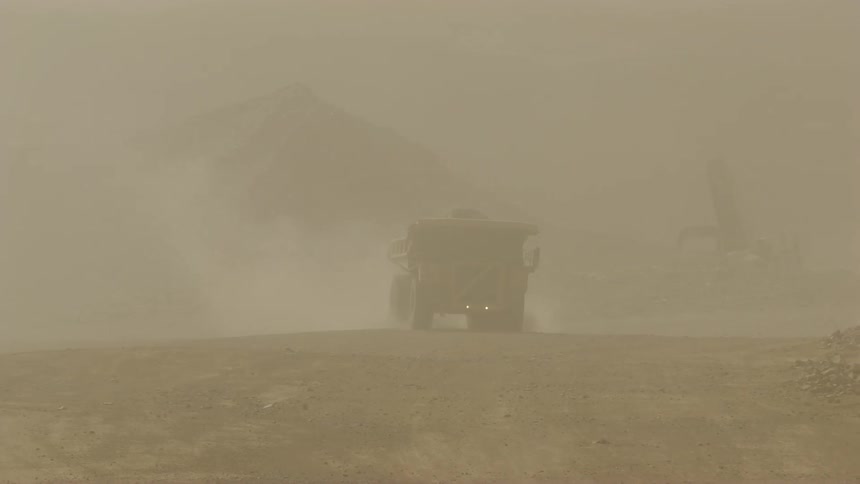 A haul truck travels on sand kicking up dust