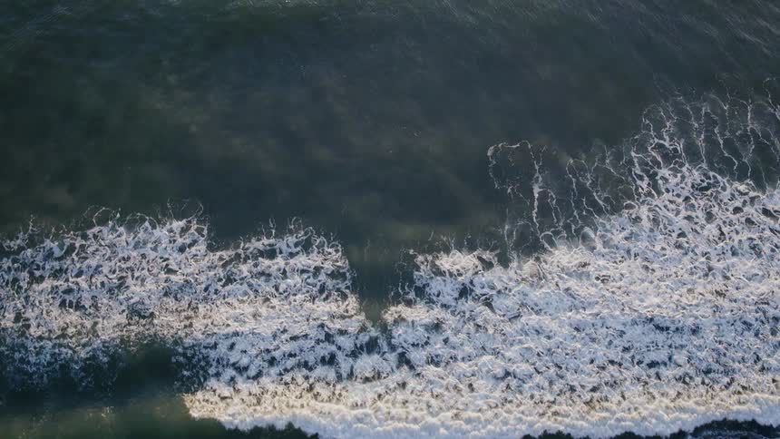 Waves roll onto a beach with surfers paddling out