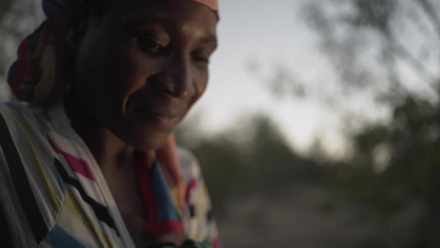 An older woman is smiling as she sits outside at dusk