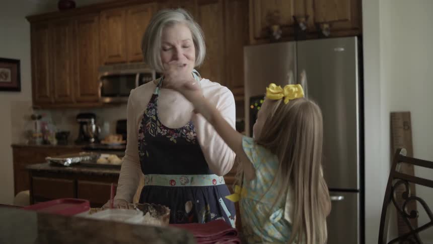 An older woman wearing an apron talks with a young girl in the kitchen