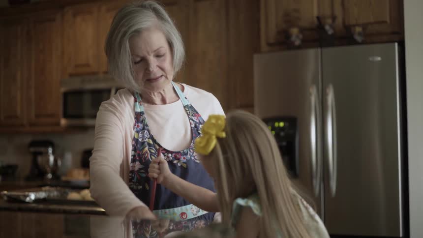 An older woman helps a young girl bake in the kitchen