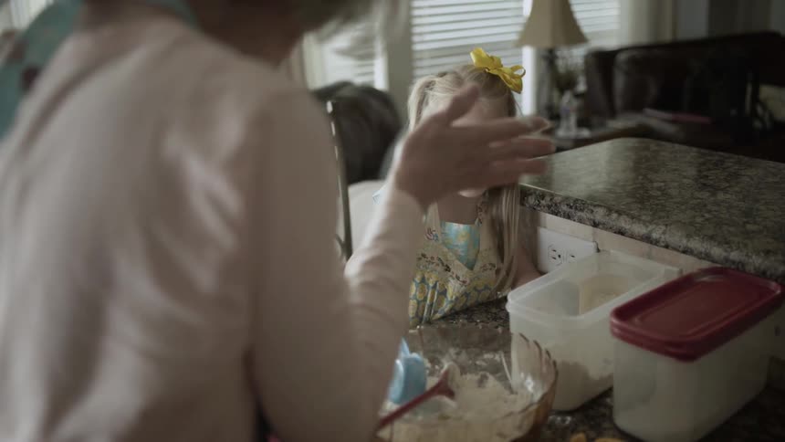 A woman puts some flour on her granddaughters face as they bake together