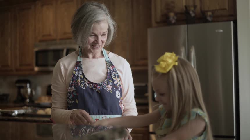 An elderly woman and a girl are baking in a kitchen during the day