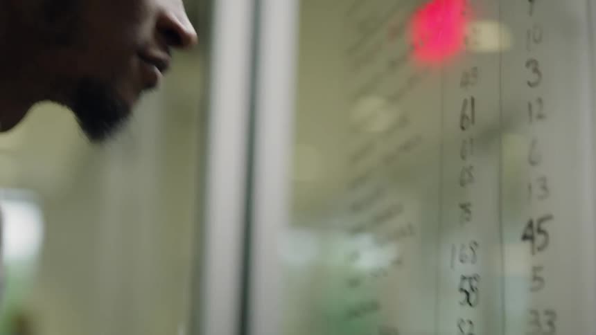 Man writing figures on a glass board using a marker