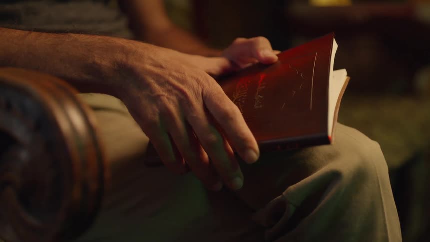 Man sitting in a chair holding a book partially opened in his lap