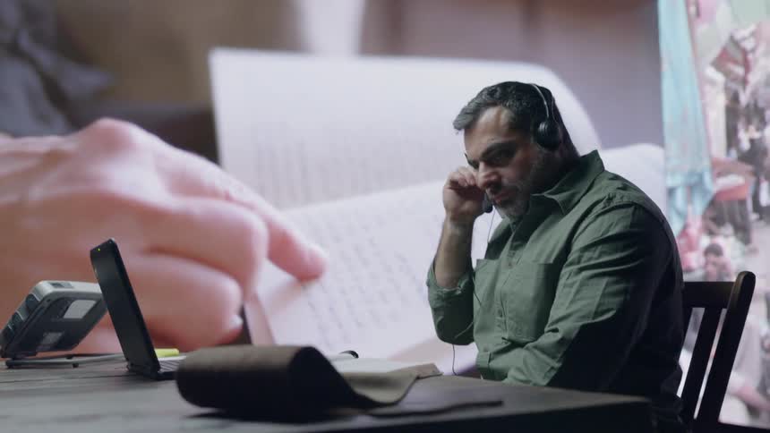 A man works at a laptop with a headset in front of LED wall