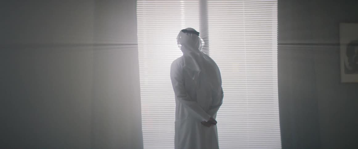 A man stands by the shades peering out