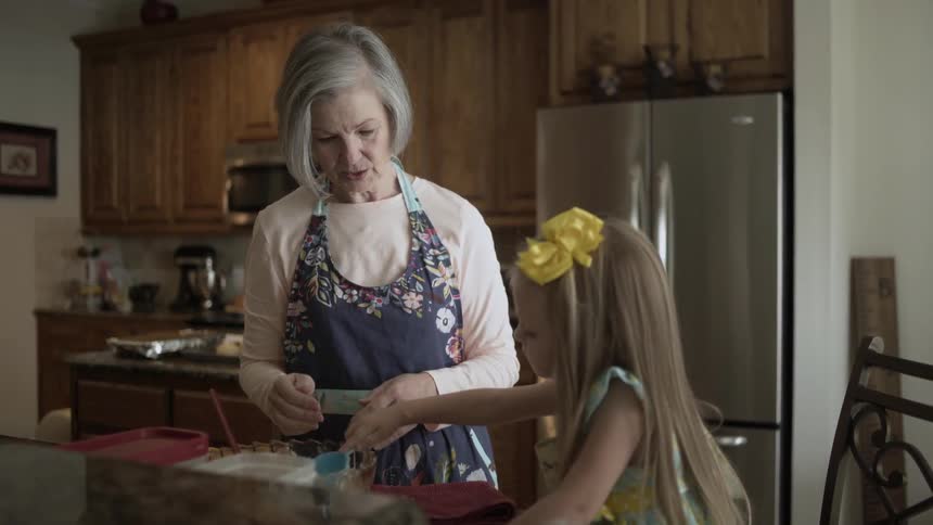 An elderly woman and a girl are baking in a kitchen during the day