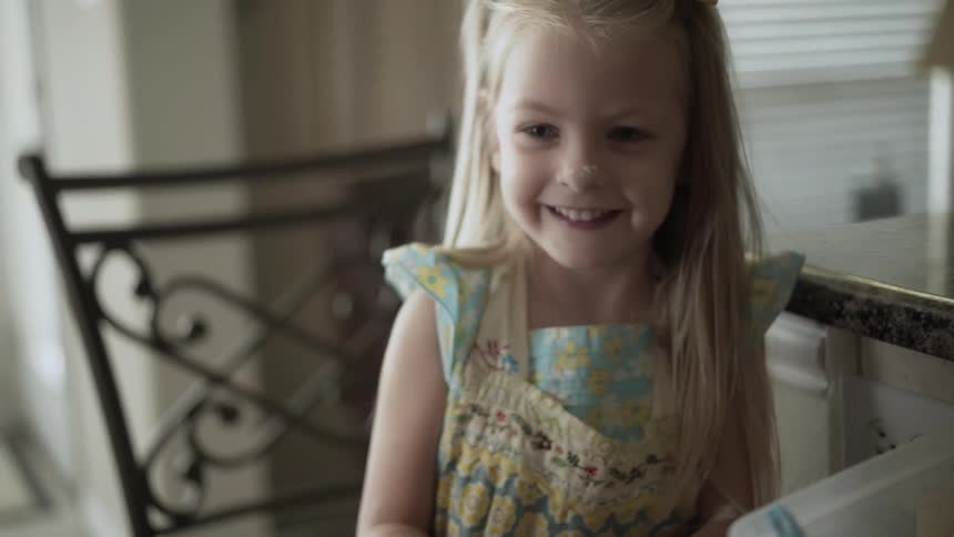 Person boops a young girl's nose as she laughs wearing a yellow bow in her hair