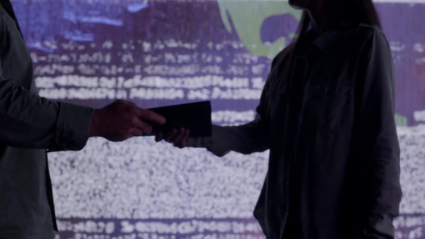 Man hands a woman a book in front of LED wall